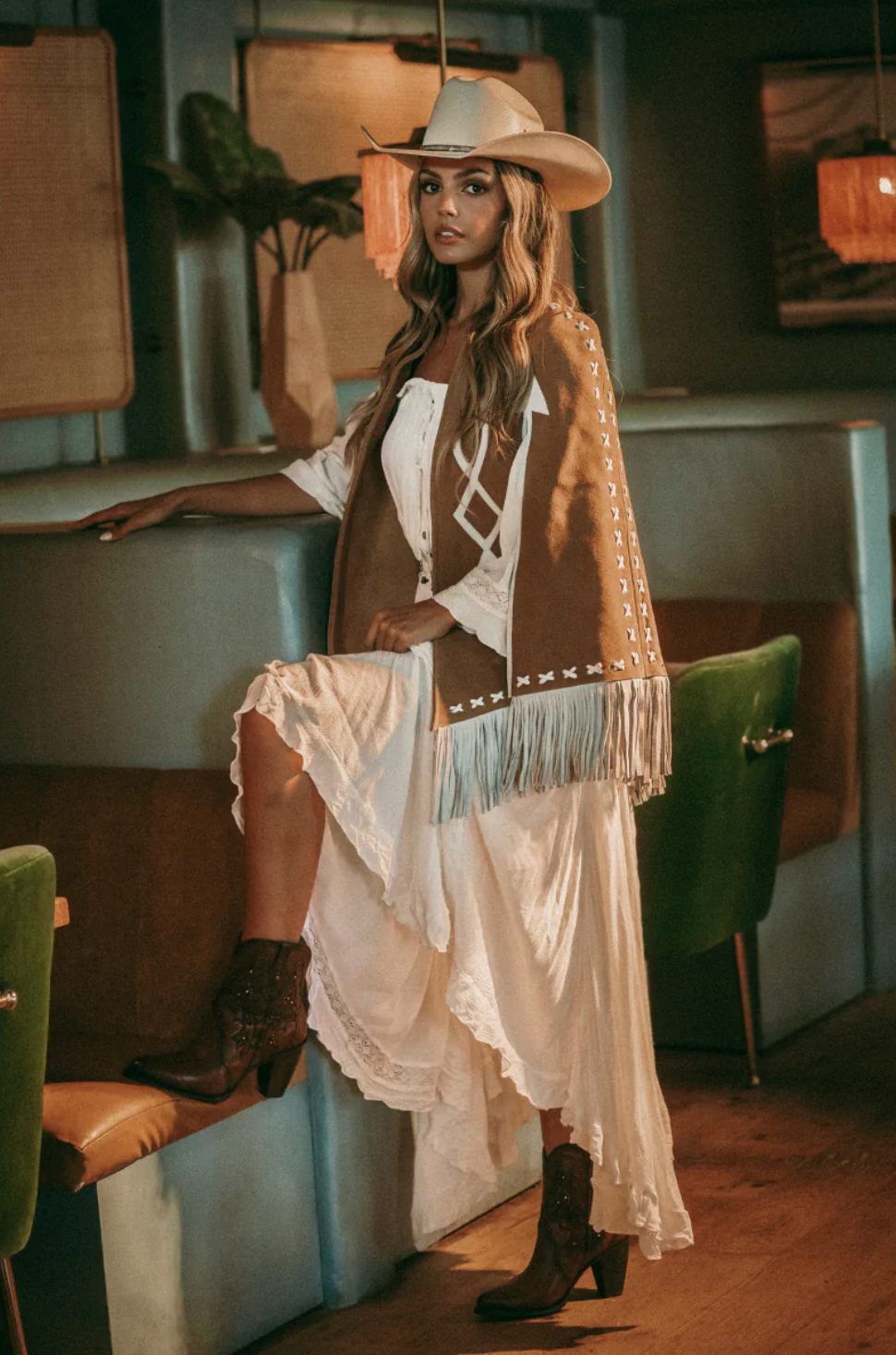 Modelo posando con estilo western, usando una tejana y vestido blanco, combinando con el Botín Urbano Venecia, decorado con brillos Swarovski y piel de color whiskey, disponible en Boot Place.