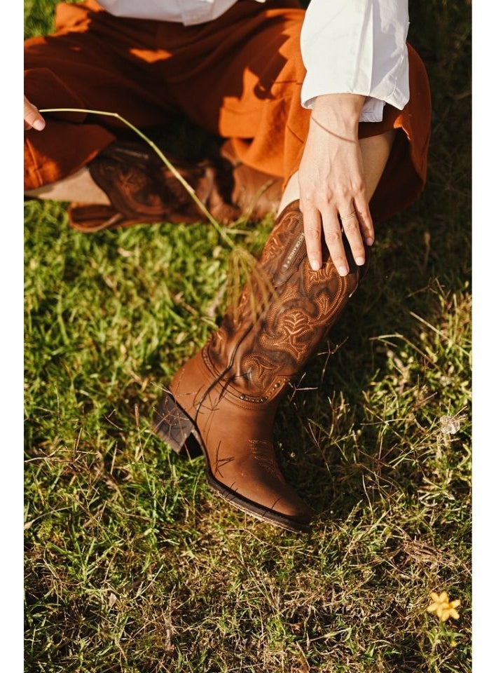 Modelo con pantalón naranja y camisa blanca, luciendo las botas vaqueras Rio Grande Samantha con bordados western y acabados en carey tan, disponible en Boot Place.