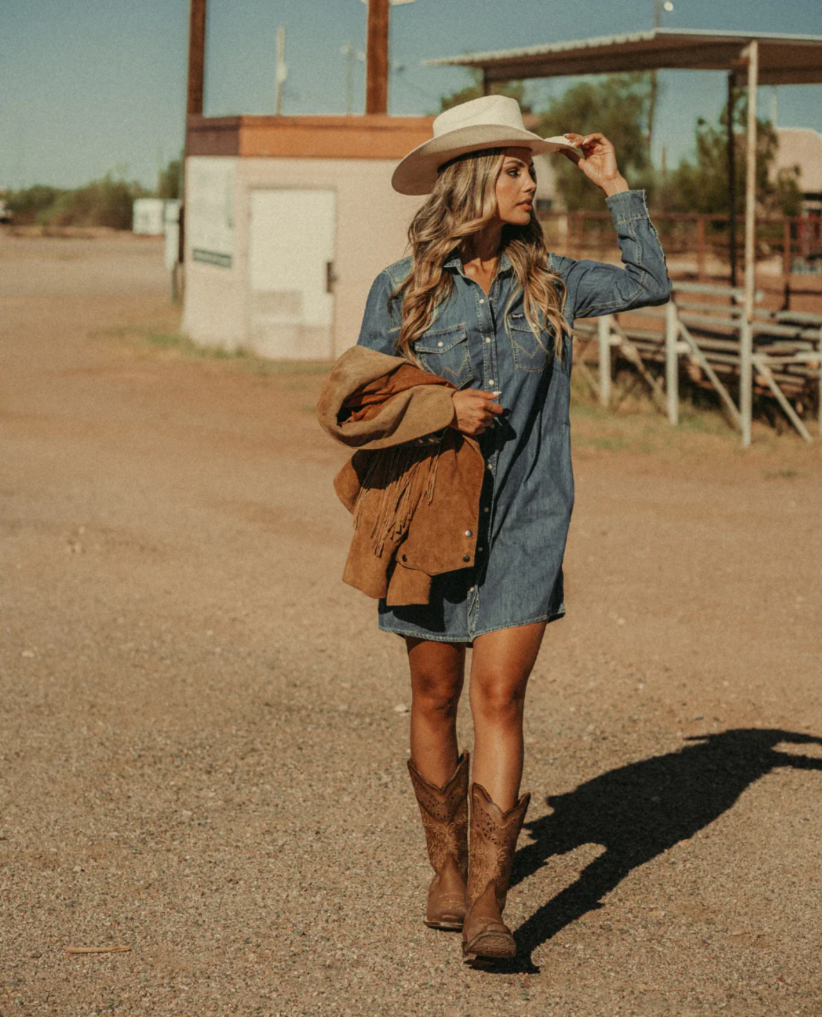 Modelo posando en un rancho con las Botas Vaqueras Alta Rio Grande Melissa, combinadas con sombrero tejano, chaqueta de mezclilla y tejanas, reflejando el clásico estilo vaquero.